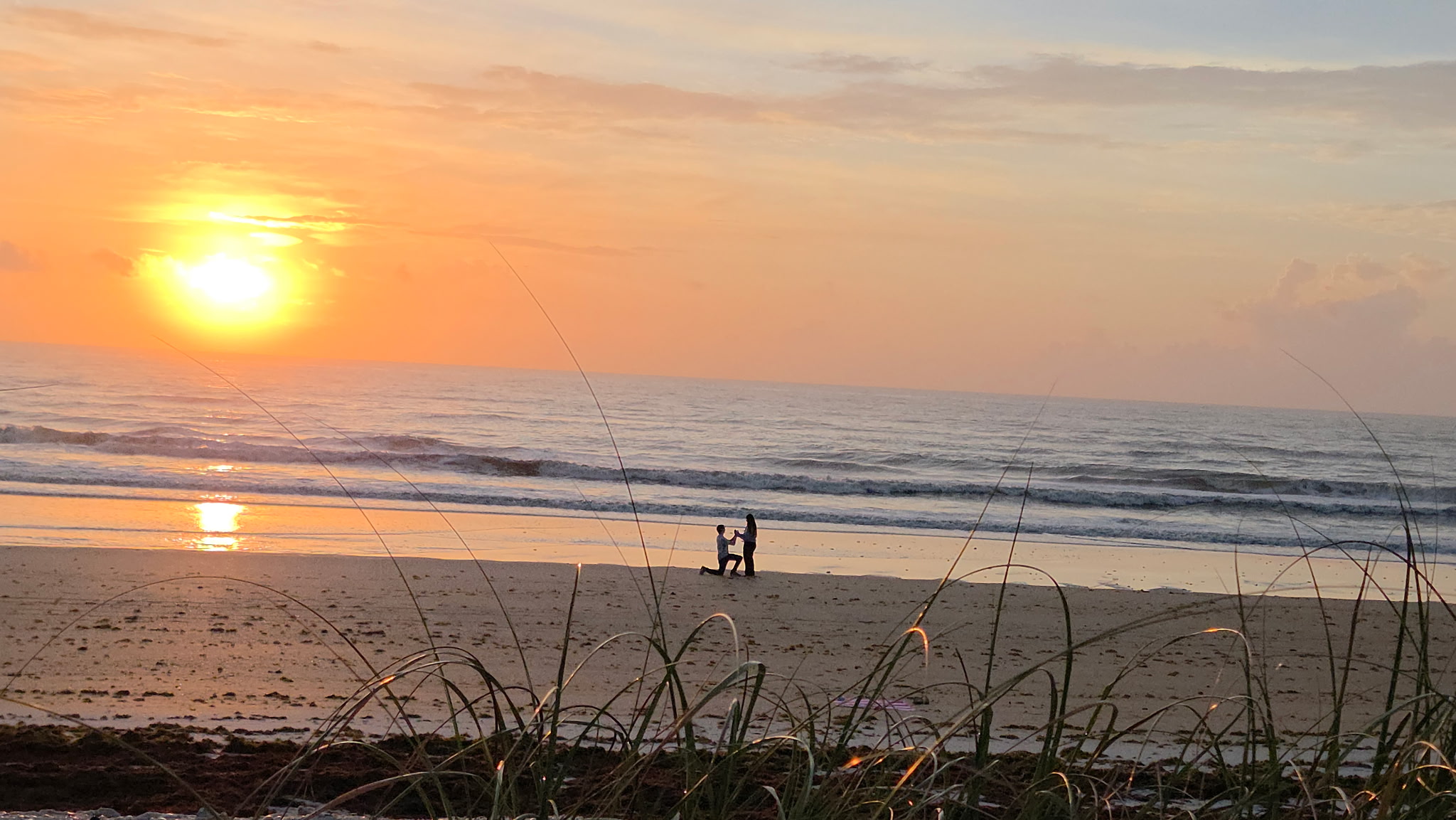 Lucas proposing to Hannah on the beach beneath a glowing sky